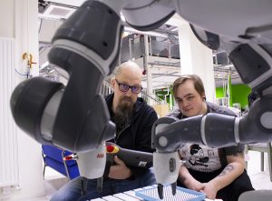 Kaksi miespuolista opiskelijaa työskentelee Yumi-robotilla.