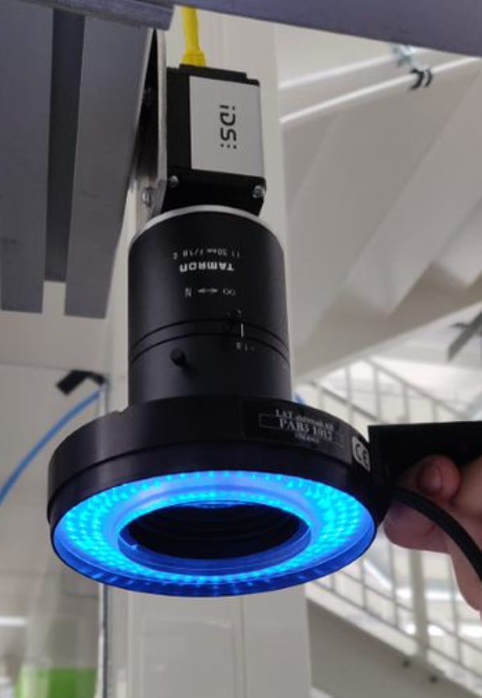 The picture shows a machine vision camera with a circular lamp around its optics.