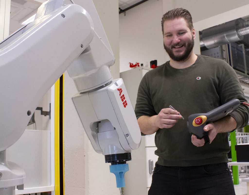 Hymyilevä mies ohjaa robottia käsiohjaimella.