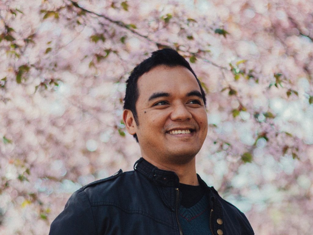 Lähikuvassa Ryann Deloso, taustalla kirsikkapuu täydessä kukassa.