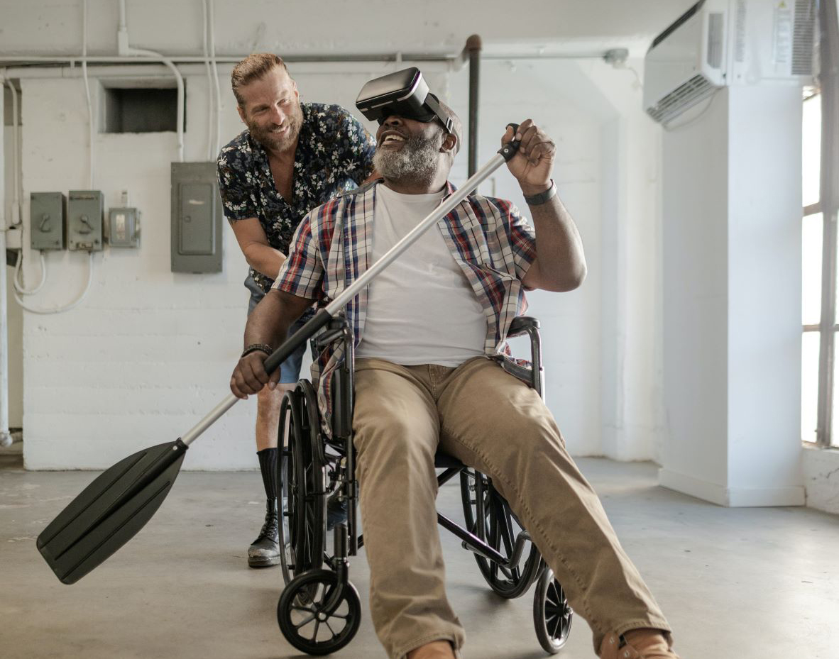 Mies istuu pyörätuolissa kädessään mela. Hänen päässään on VR-lasit.
