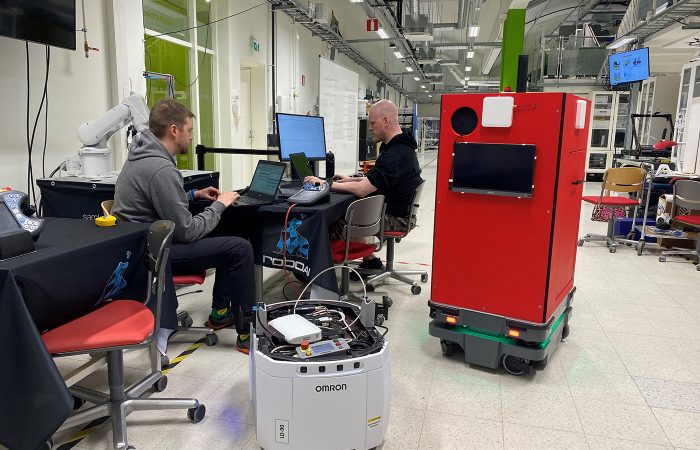 Kaksi miestä työskentelee, etualalla kaksi mobiilirobottia.