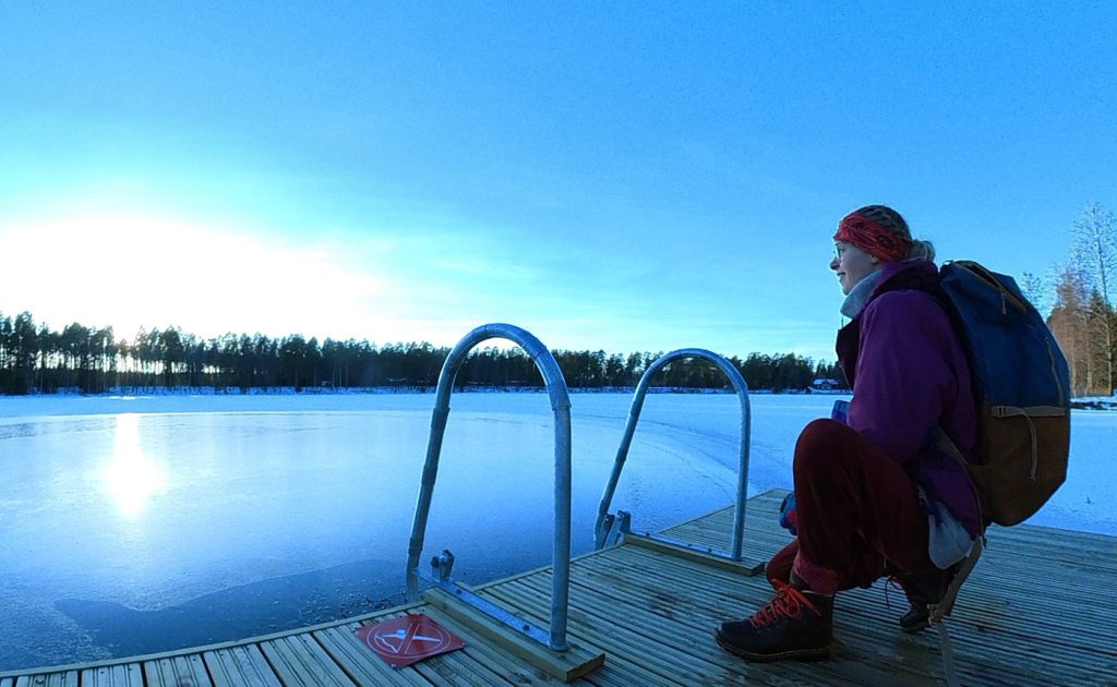 Nainen on kyykyssä laiturilla jäisen järven rannalla.