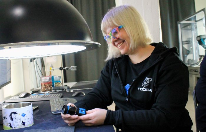 Robotiikka Akatemia 23.11. 14 1 Vaaleahiuksinen naisopiskelija hymyilemässä, käsissään konenäkökamera.