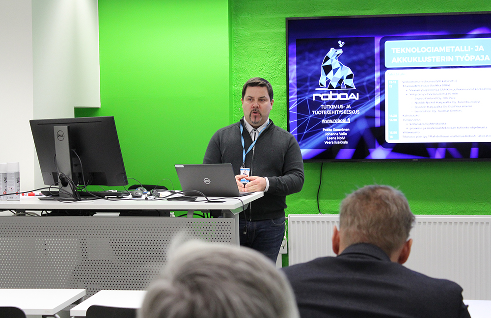 Mies seisoo muiden edessä ja esittelee materiaaliaan.