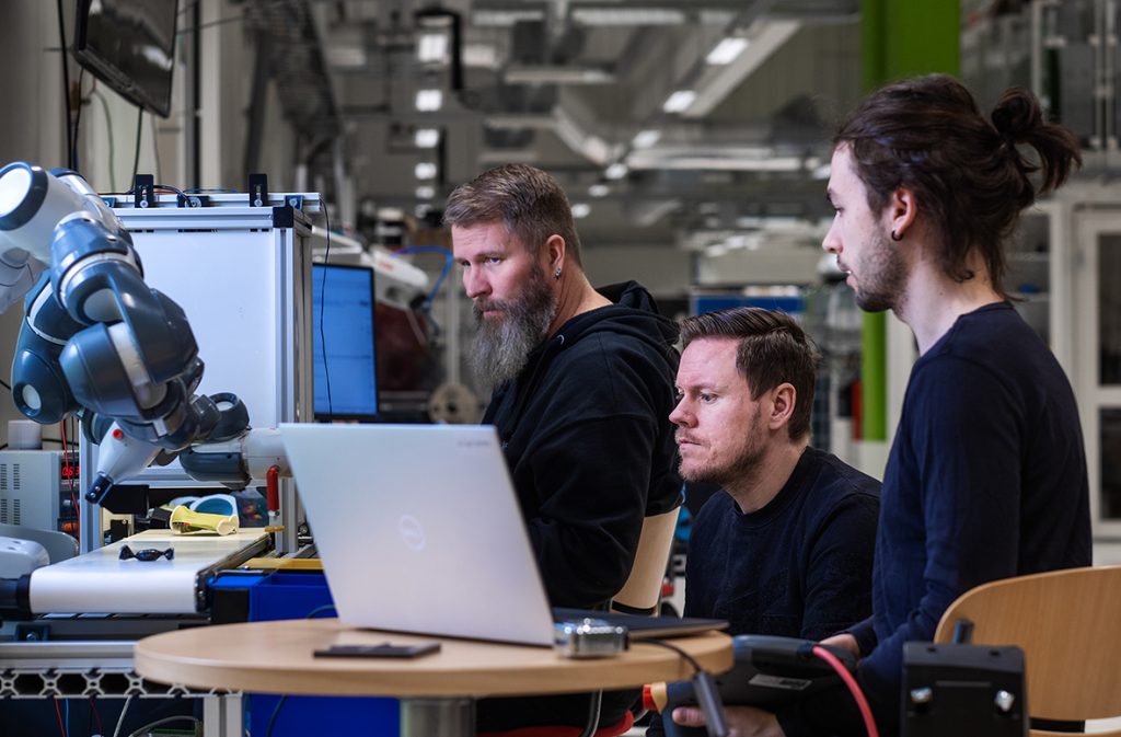 Kuvassa kolme miespuolista RoboAI-akatemian opiskelijaa työskentelee koneella.