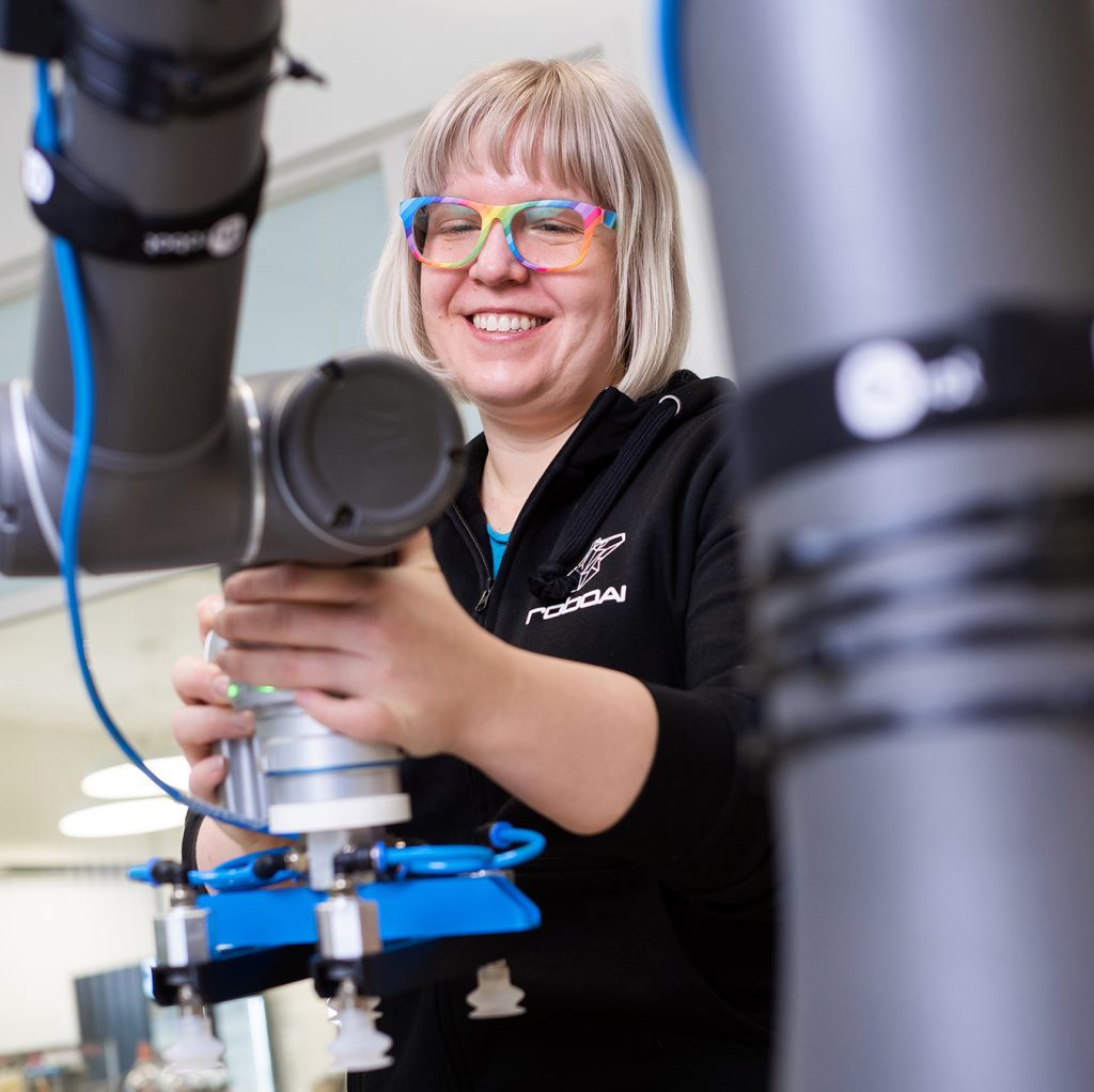 A young woman wearing colourful glasses uses a collaborative robot.