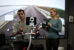 Kuvassa mieshekilö istuu pelituolissa ja nainen vieressä pitää käsissään VR-laseja.