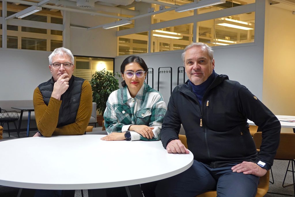 Tarmo Lipping, Reijo Koivula and Matin Beiramvand sit at a white table and look at the camera.