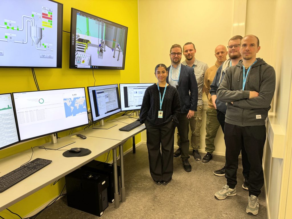 Kuvassa RoboAI Cyberlabin projektityöntekijät. He seisovat monitorien vieressä.