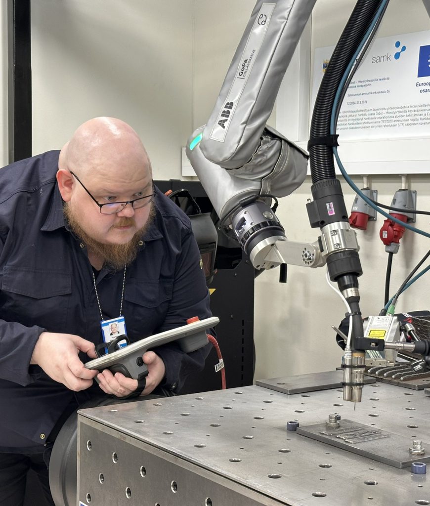 A man tests a welding robot and holds the controller in his hand.