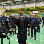 Eksoskeletonit Man dressed in exoskeleton showcasing it to company representatives