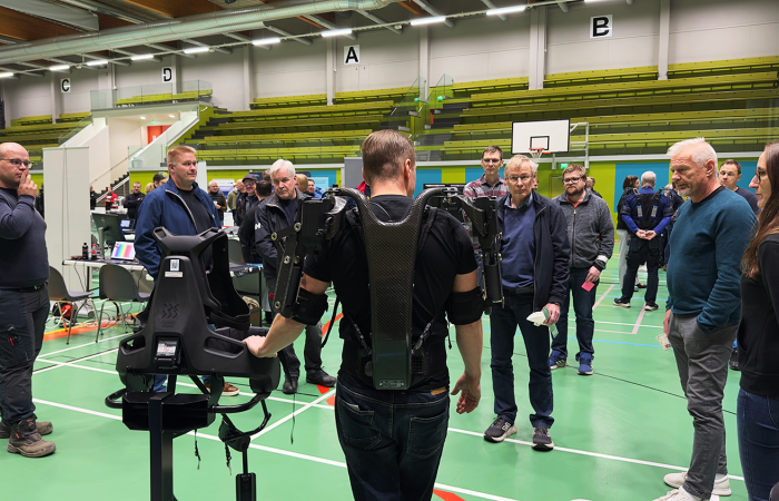 Eksoskeletoniin pukeutunut mieshenkilö esittelee eksoja ympärilleen keräytyneelle yleisölle
