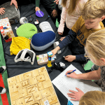 Funteeraamo salkkutehtävä2 Ryhmä lapsia tunnistaa pöydälle aseteltuja hyvinvointiteknologioita