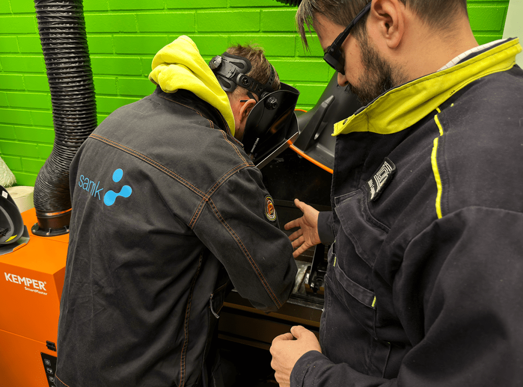 Mieshenkilö opastaa osallistujaa laserhitsauksessa.