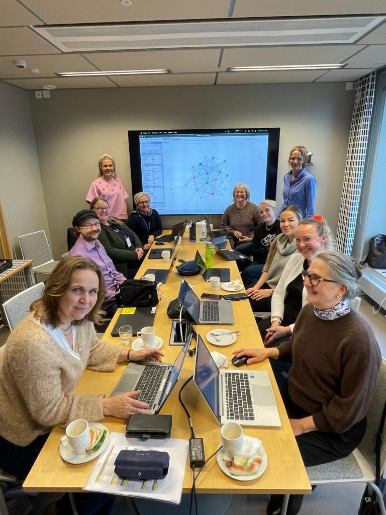 Pitkän pöydän ympärillä on henkilöitä läppäreiden kanssa.