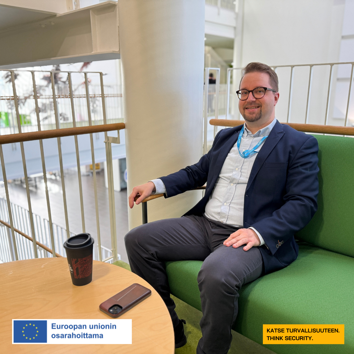 Pikkutakissa oleva silmälasipäinen mies katsoo hymyillen kameralle. Pöydällä ovat hänen kännykkänsä ja puhelin. Hän istuu vihreällä sohvalla Satakunnan ammattikorkeakoulun tiloissa.