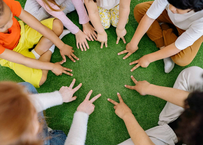 Lapset istuvat ringissä ja heidän kätensä ovat ringin keskellä, vihreällä matolla.