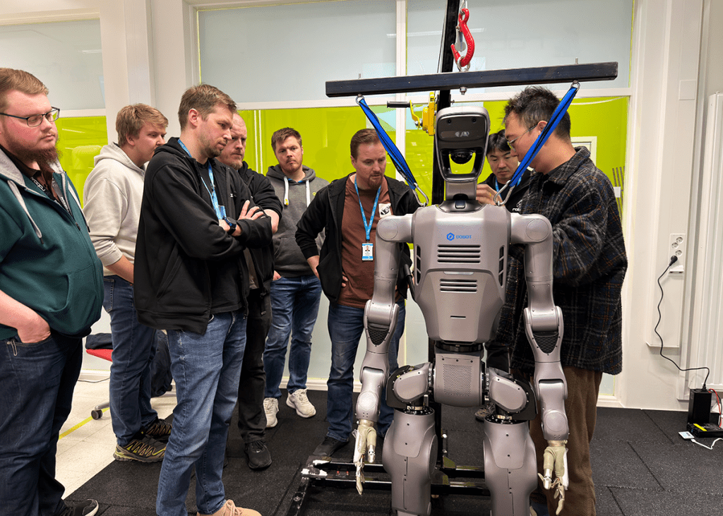 Joukko opiskelijoita ja asiantuntijoita kerääntyneenä humanoidirobotin ympärille.