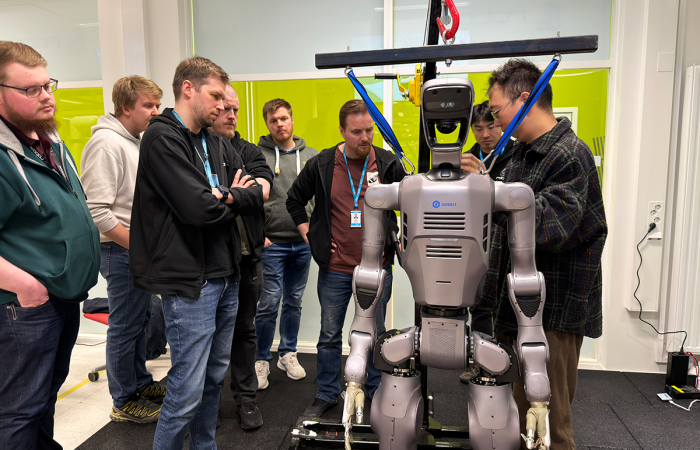 Joukko opiskelijoita ja asiantuntijoita kerääntyneenä humanoidirobotin ympärille.