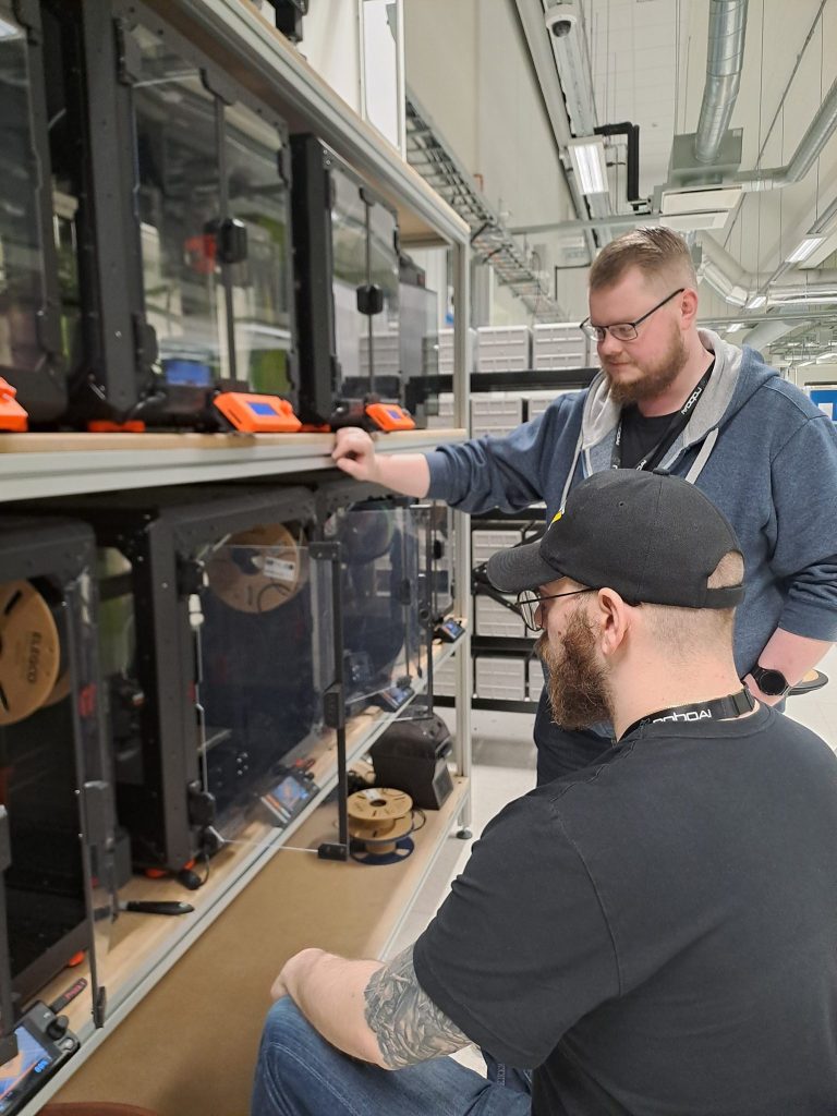 Two people inspecting 3D printers at a workstation in a laboratory.
