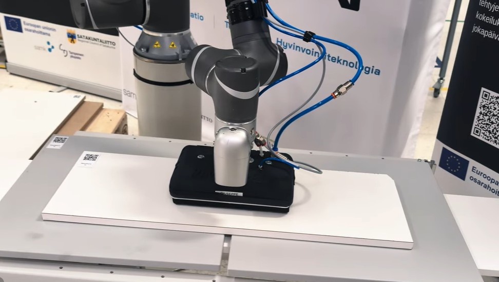 Robottikäsivarsi käsittelee tuotetta automaatiolaitteella.