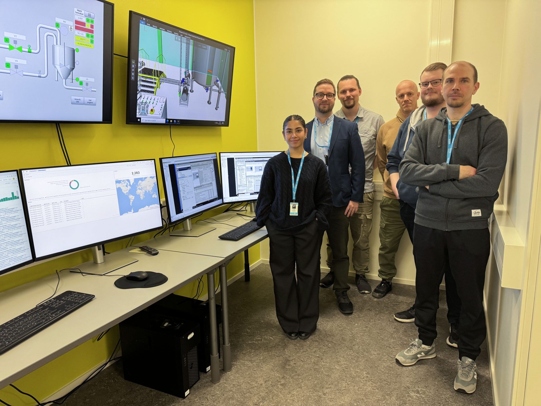 Kolme nuorta kesätyöntekijää sekä lehtorit ja laboratorioinsinööri seisovat RoboAI Cyberlabissa ja hymyilevät kameralle.