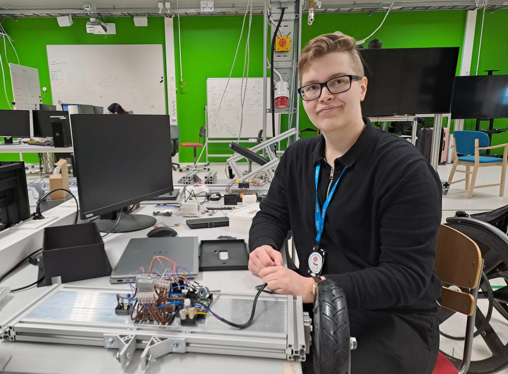Henkilö esittelee elektroniikkarakennelmaa työpisteessä laboratoriossa.