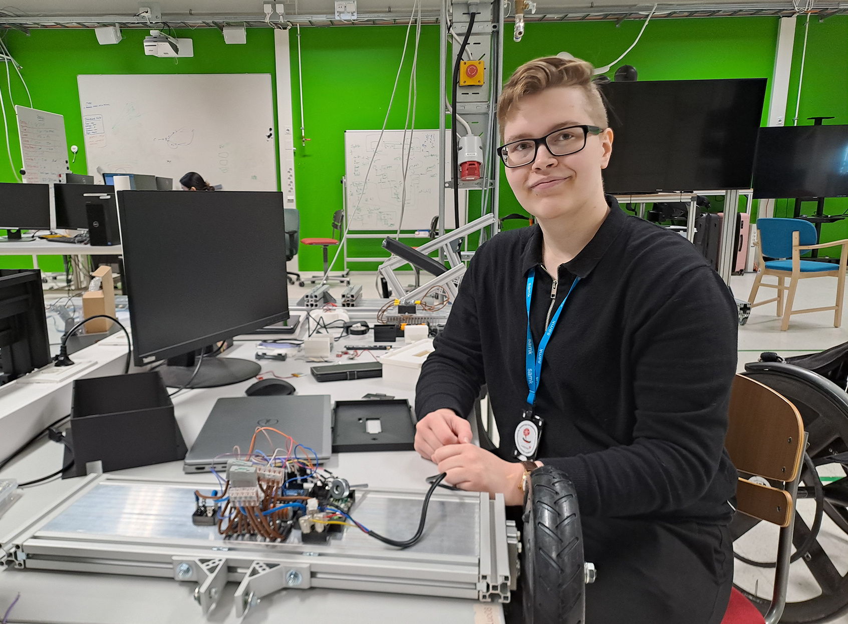 Henkilö esittelee elektroniikkarakennelmaa työpisteessä laboratoriossa.