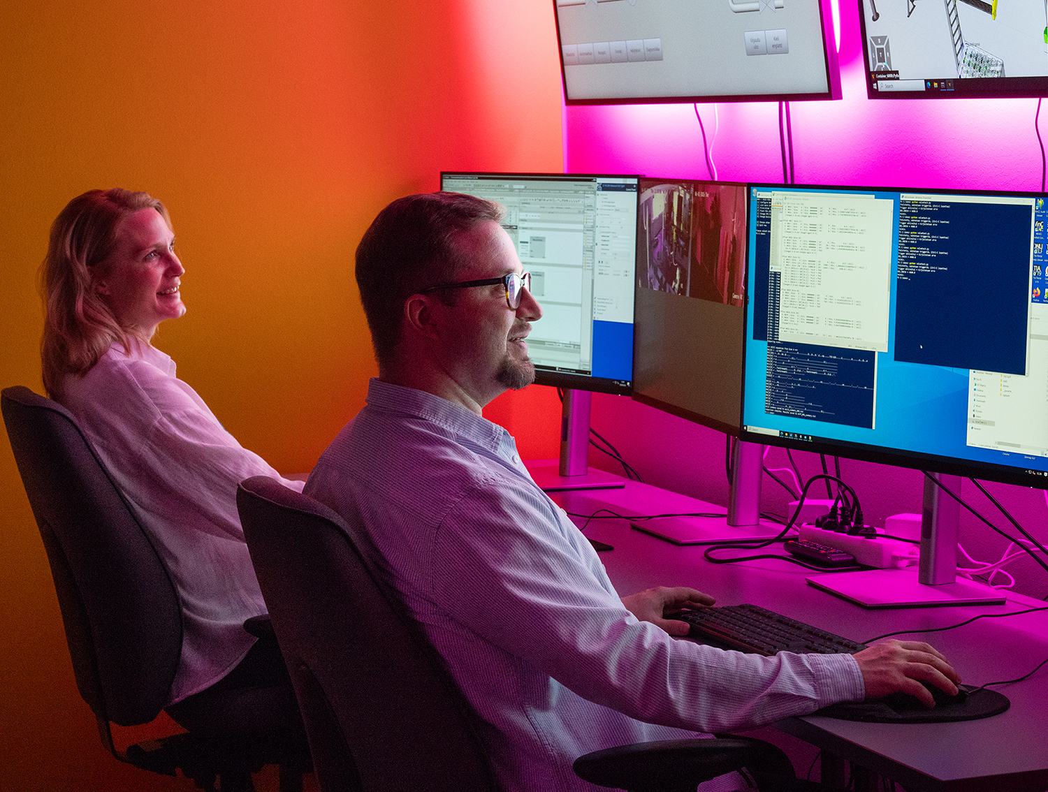Two people in the Cyberlab are smiling while looking at computer screens.