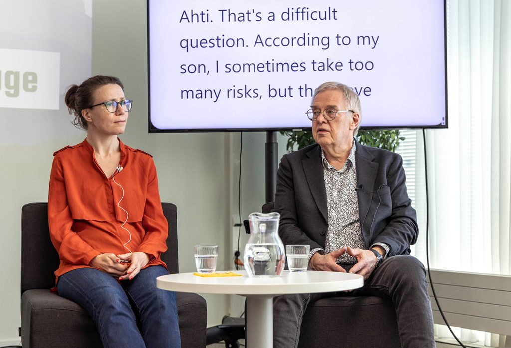 A woman and a man are sitting in front of a large screen.