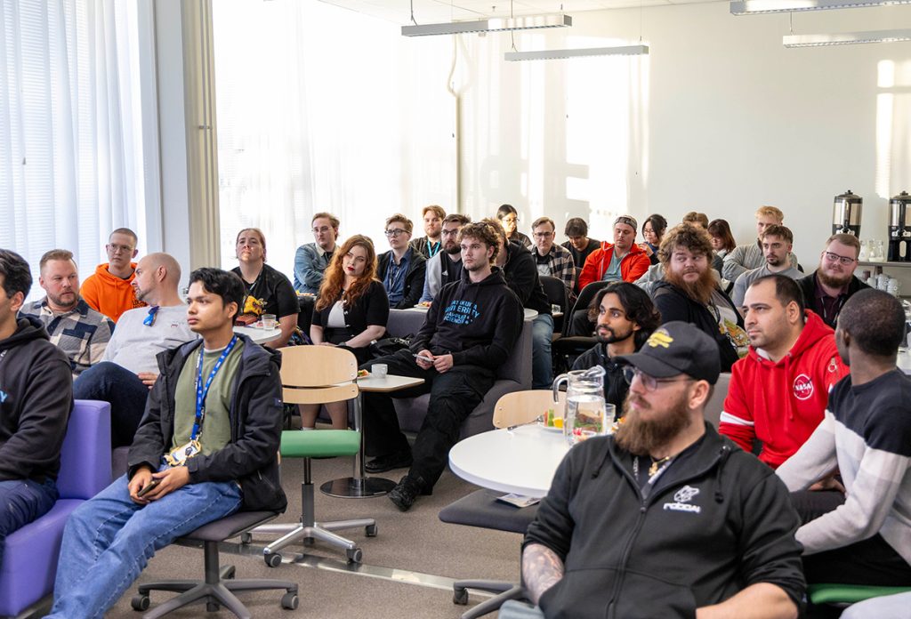 A large group of students is sitting in a well-lit classroom.