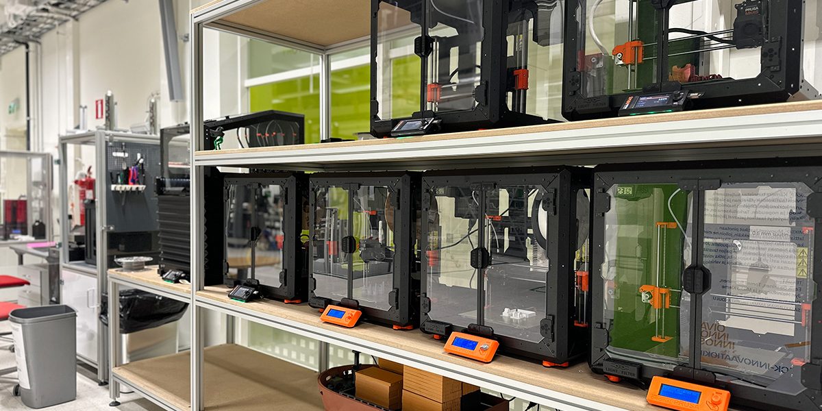 A metal shelf with rows of black 3D printers on its shelves.