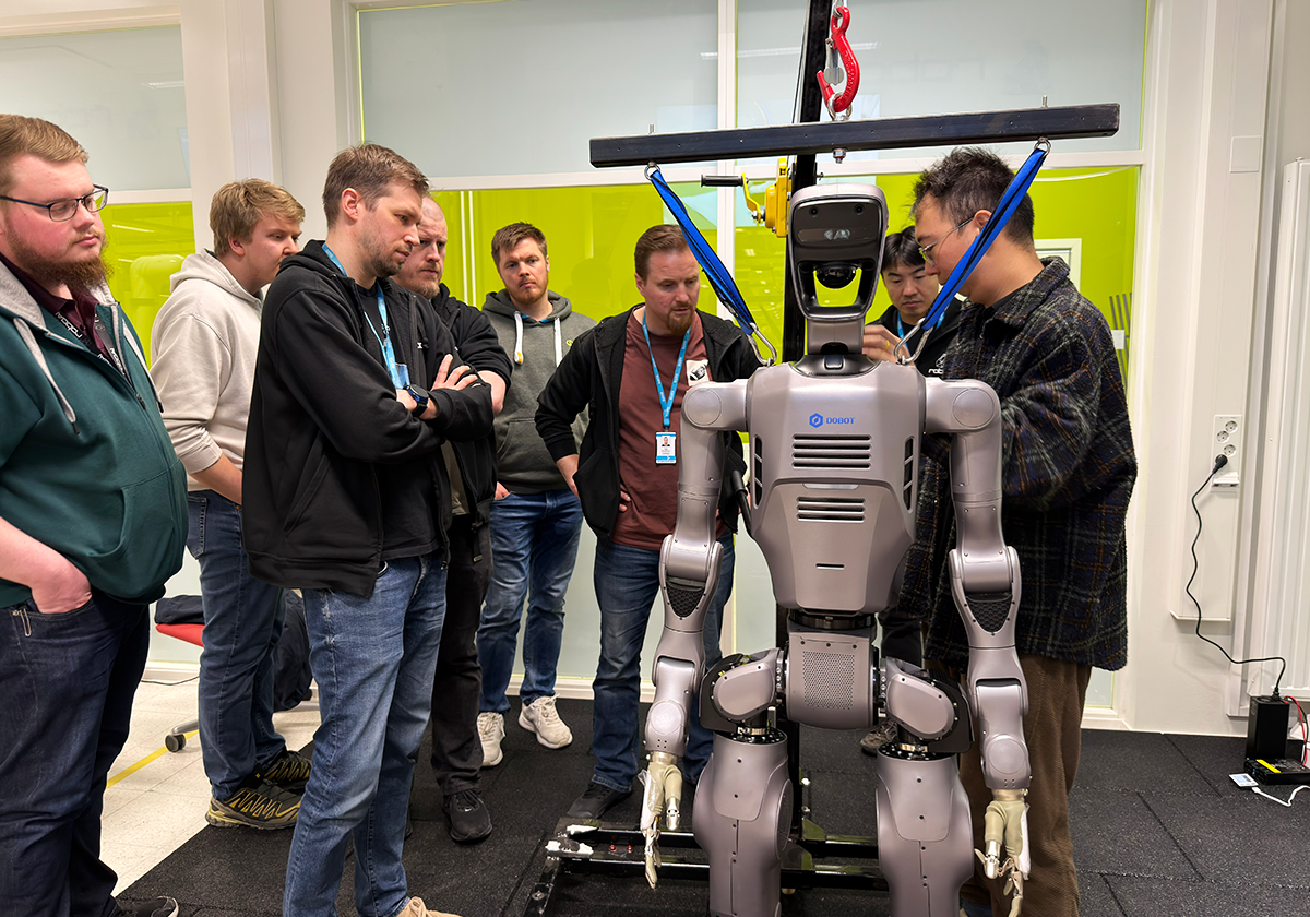 A group of researchers and students gathered around a gray humanoid robot.