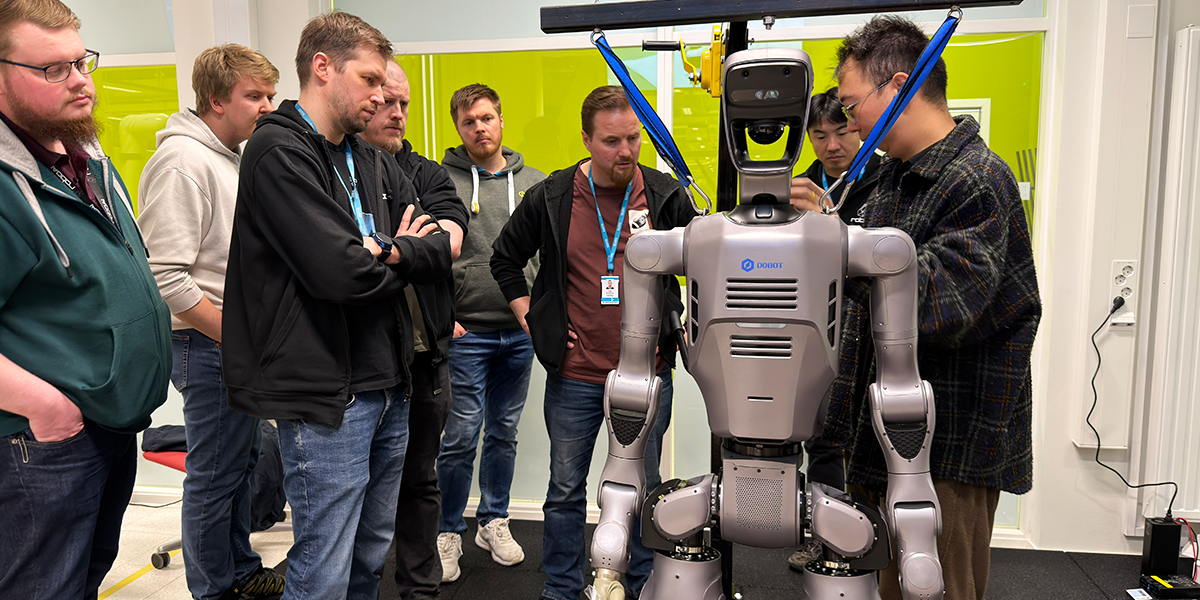 Joukko opiskelijoita ja asiantuntijoita kerääntyneenä humanoidirobotin ympärille.