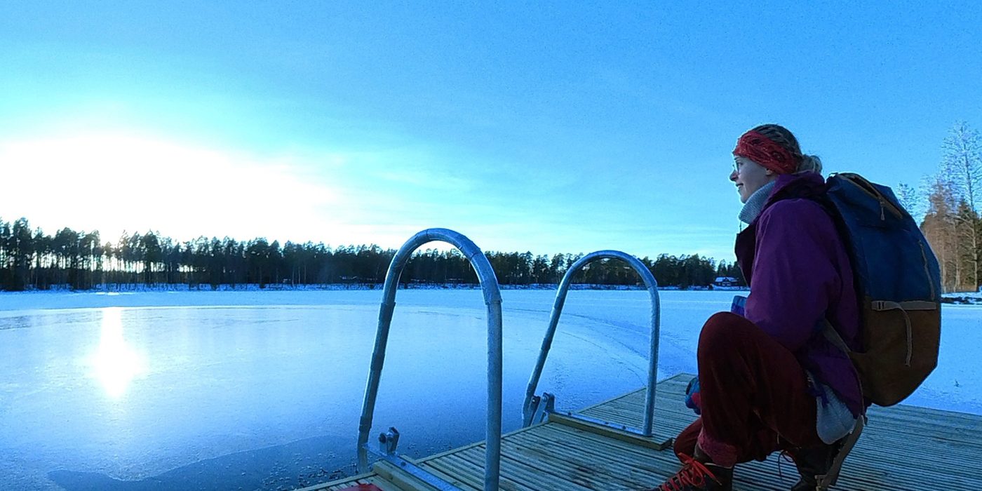 Nainen on kyykyssä laiturilla jäisen järven rannalla.