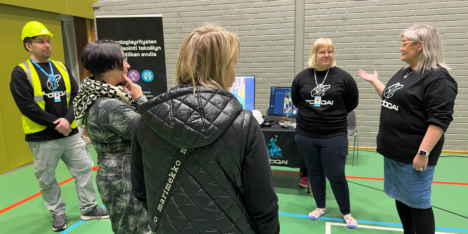 Kaksi naishenkilöä tutustumassa ständin sisältöön kolmen henkilön esittelemänä