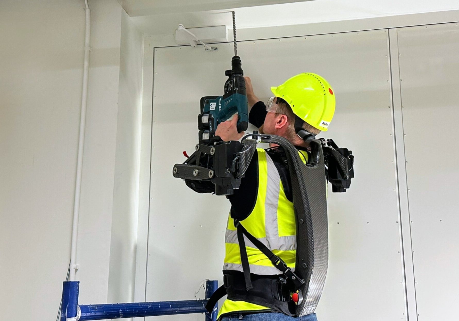 B422e4e1 Aaa6 4848 B990 4c354f6a49a1 A man working overhead with a drill dressed in an exoskeleton